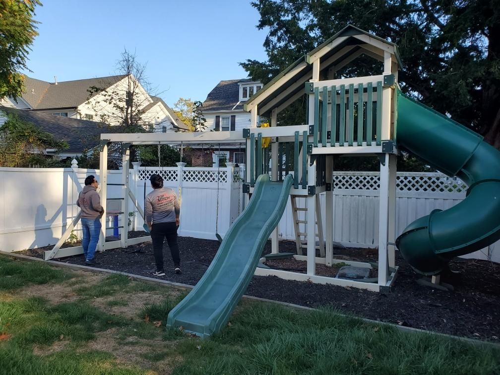 Two people are standing in front of a playground with a green slide.
