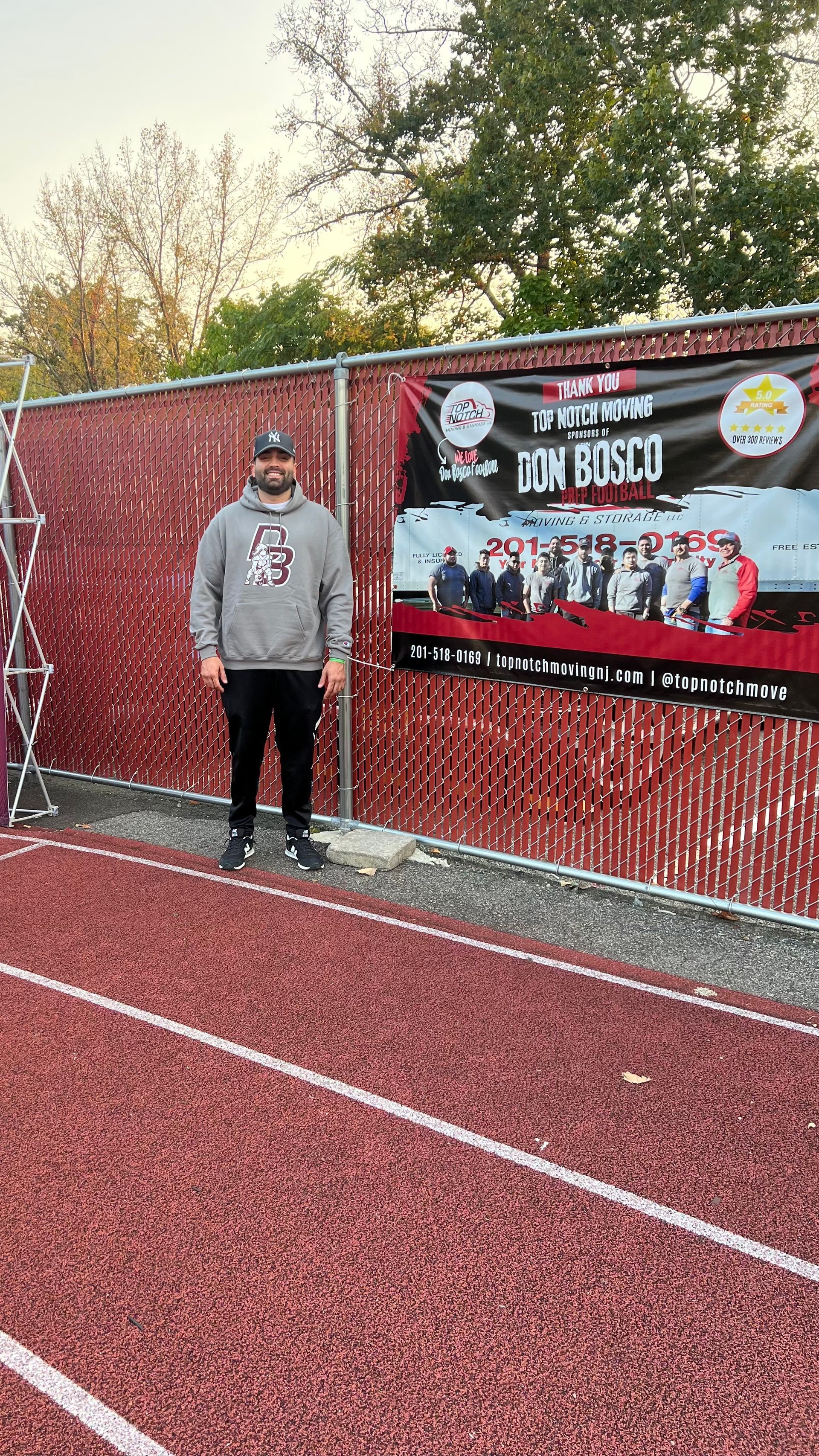 A man is standing on a track in front of a fence.