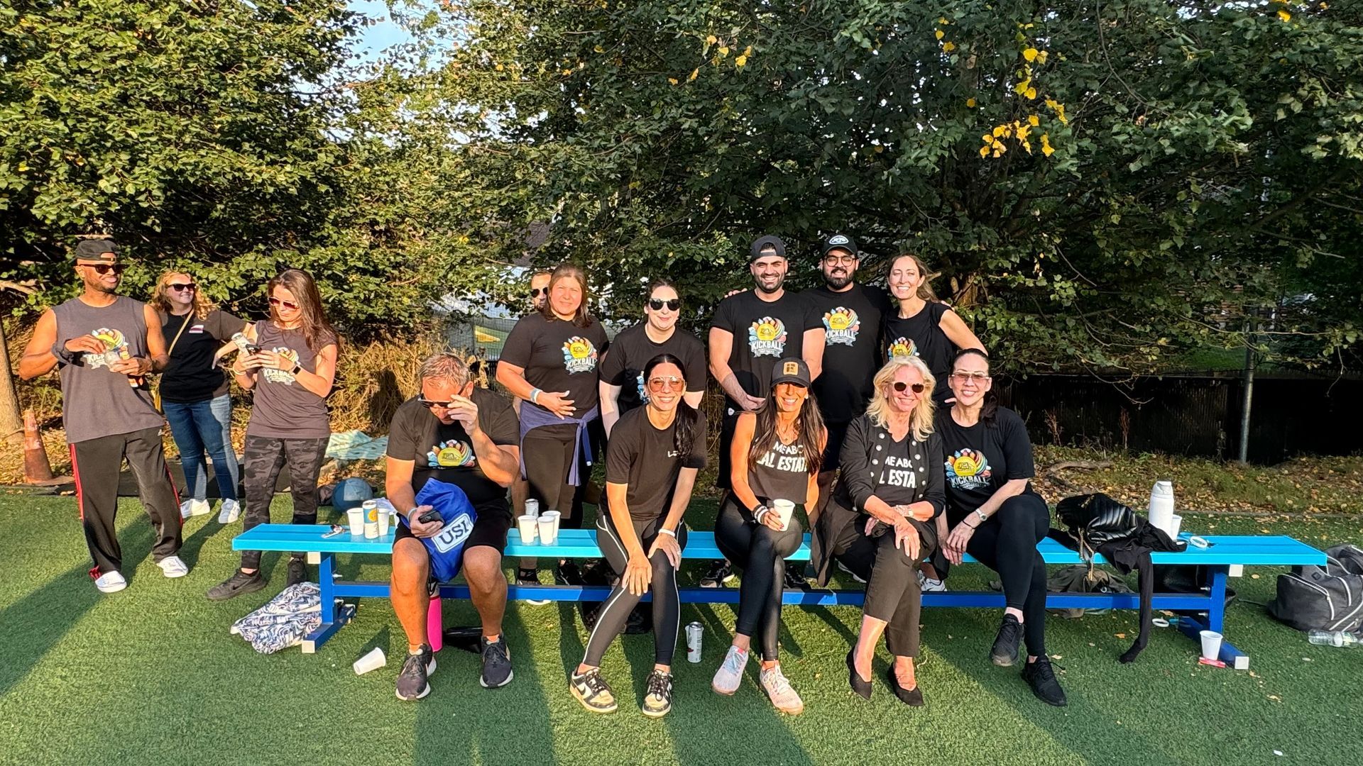 A group of people are sitting on a blue bench in a field.