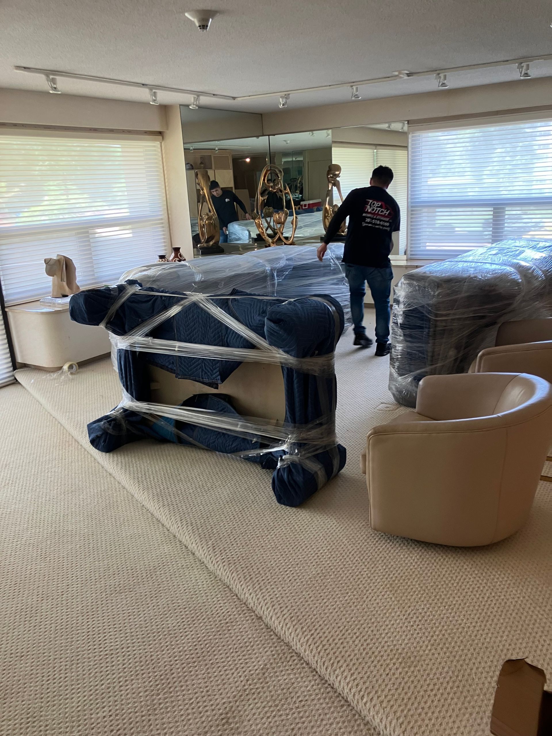 Movers wrapping furniture in plastic, preparing for a move inside a home.