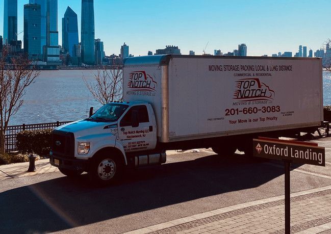 A white moving truck is parked on the side of the road in front of a city skyline