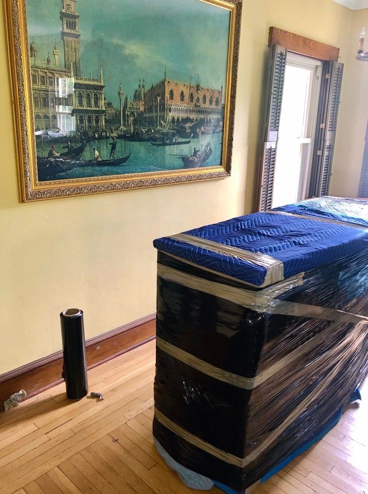 A room with a painting on the wall and a trunk wrapped in plastic