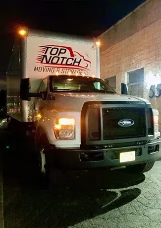 A white moving truck is parked in front of a building at night