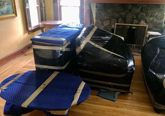 A living room with furniture wrapped in plastic and tape