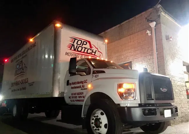A top notch moving truck is parked in front of a building at night