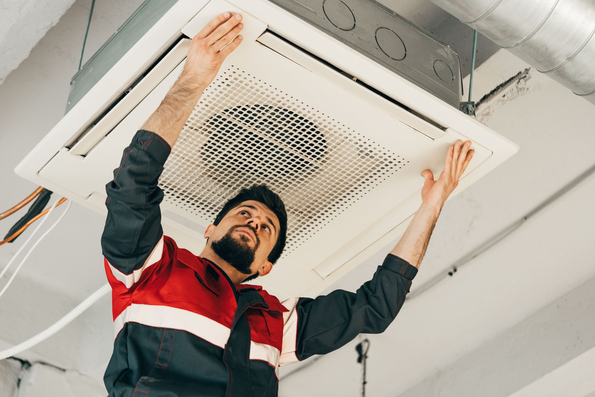 Man in work clothes installing ceiling air conditioning unit.