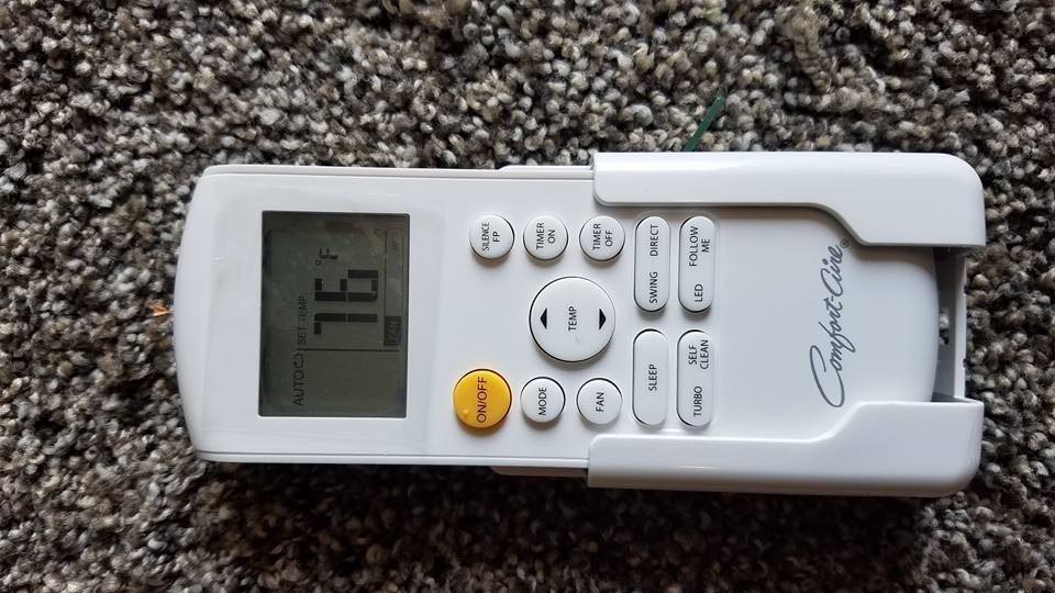 White Comfort Care air conditioner remote control on a textured carpet, showing a temperature of 76 degrees.