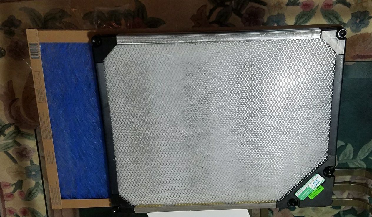 A metal vent with a black frame and a blue air filter next to it.