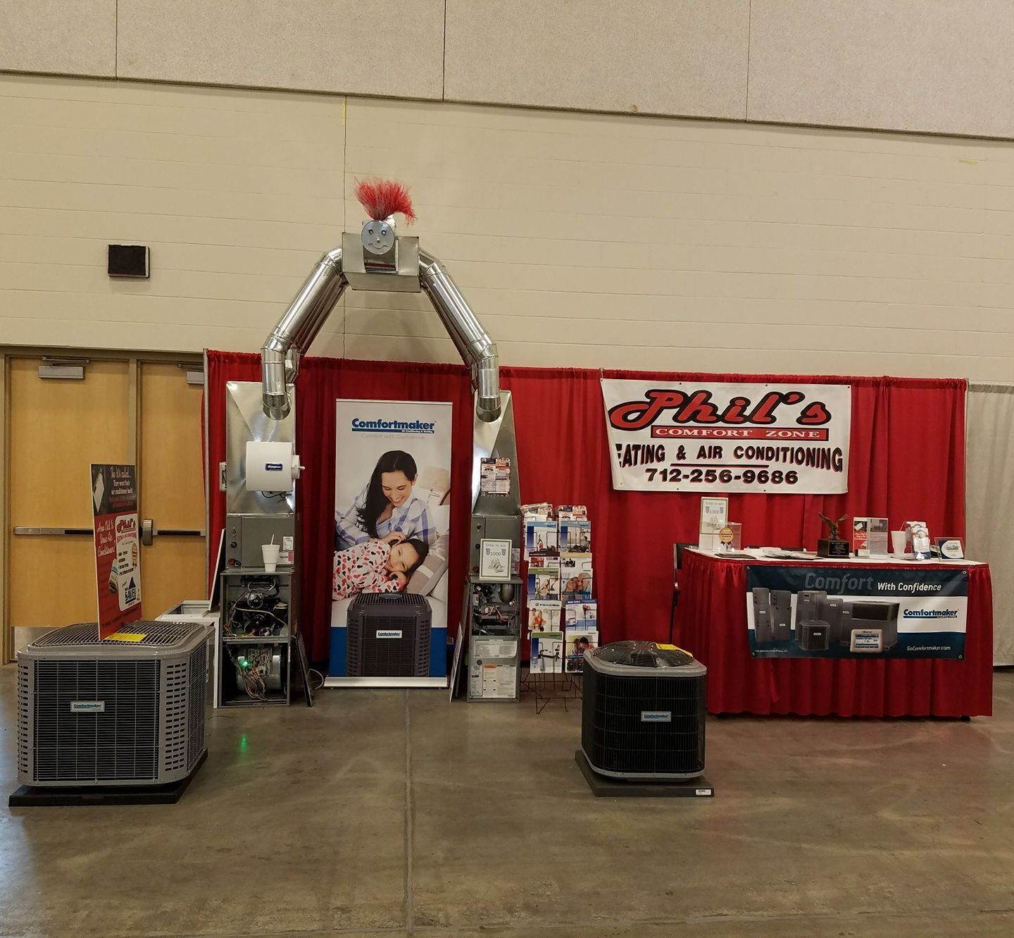 HVAC booth at an event. Exhibits include air conditioners, heaters, and promotional materials. Red backdrop.