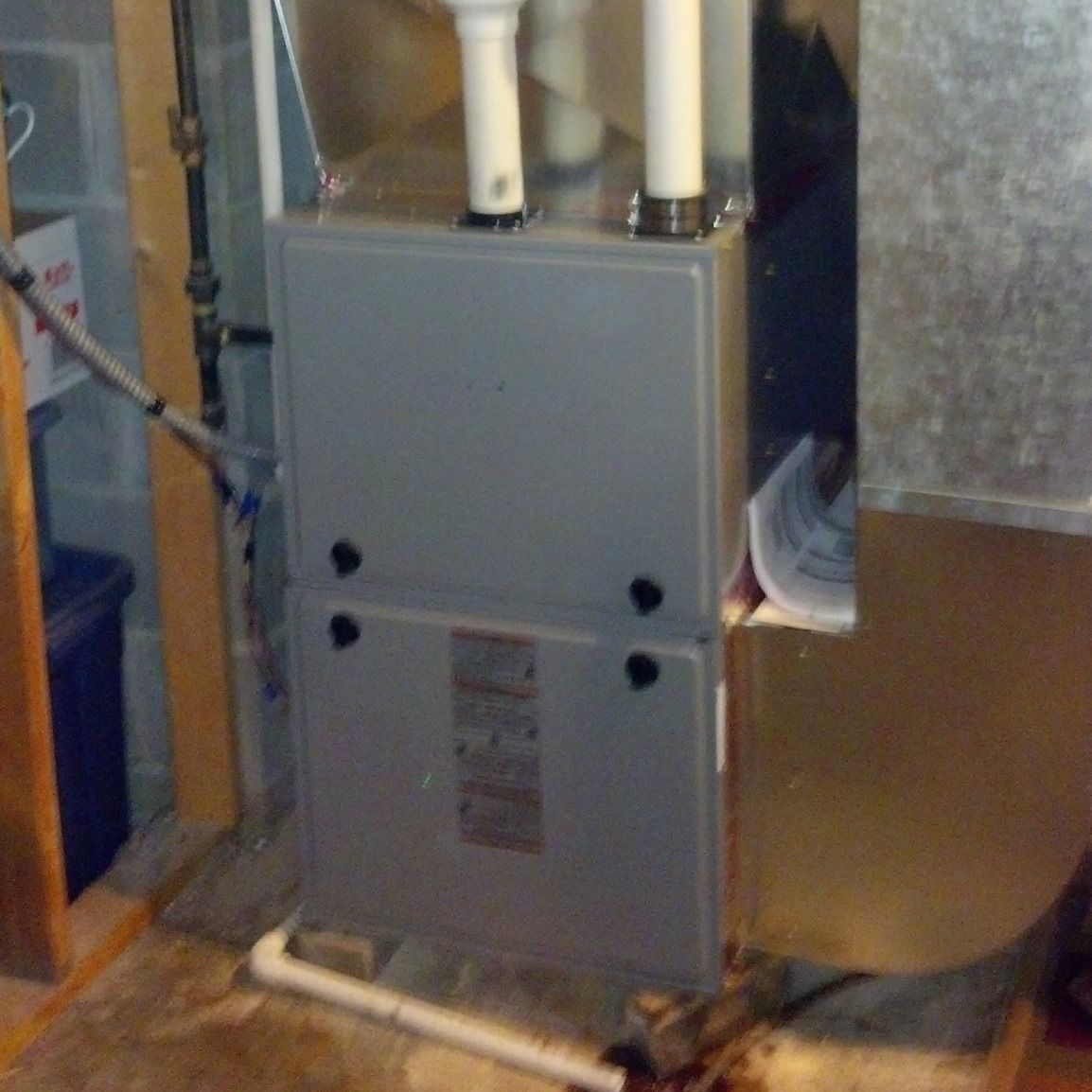 Furnace in a basement, with two white exhaust pipes and a gray metal cabinet.