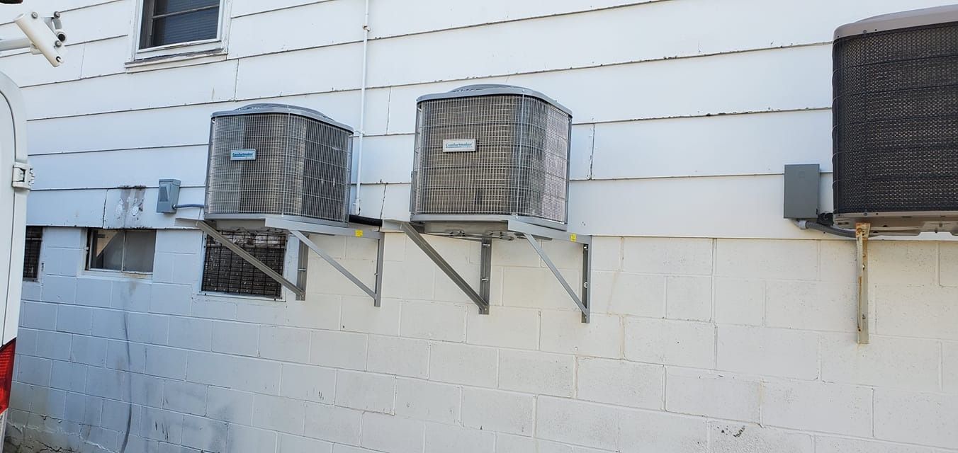 Three air conditioning units mounted on a white brick wall.