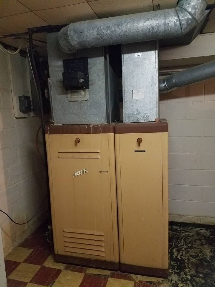 Furnace in a basement. Beige metal cabinet with ventilation, vent pipes, and a checked floor.