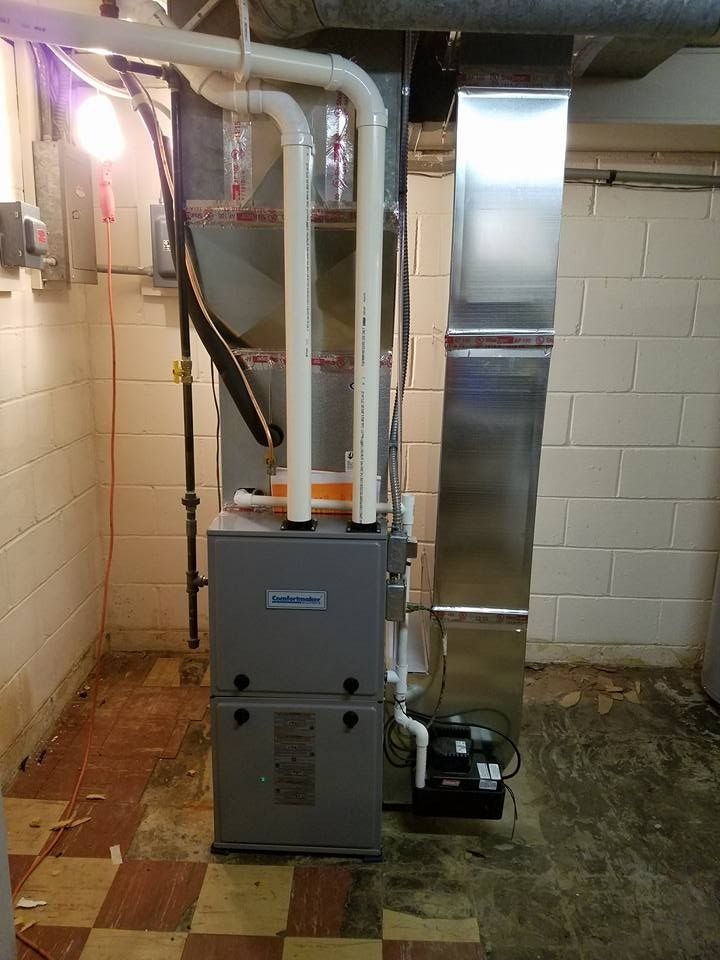 Furnace in a basement setting with white pipes and silver ductwork. Brick-pattern floor.