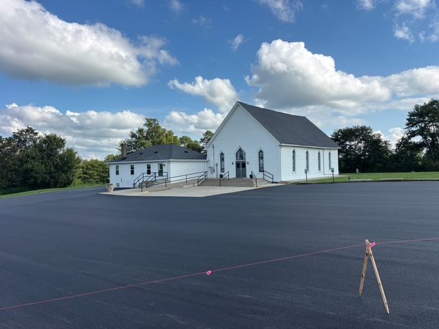 White church with steeple beside an empty parking lot under a partly cloudy sky