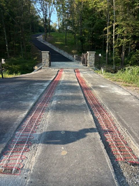 Bridge deck with red inlaid tracks leading to a narrow forest road beyond stone pillars
