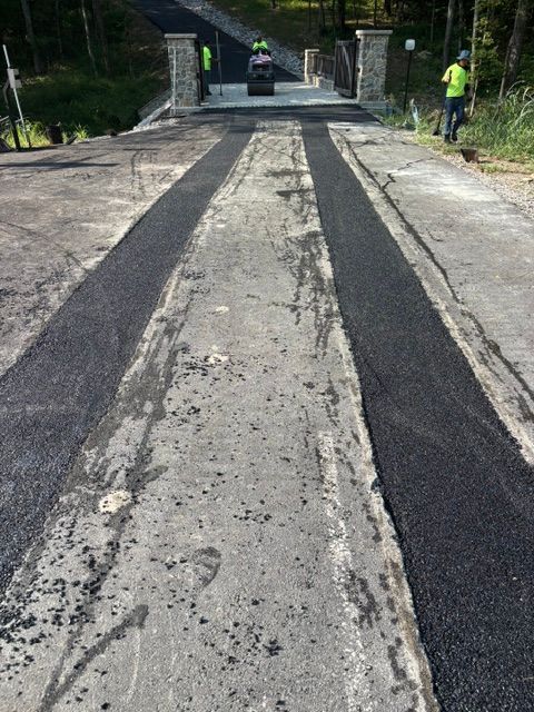 Damaged concrete road leading to a bridge, with dark asphalt strips and a worker in a neon vest on the right.