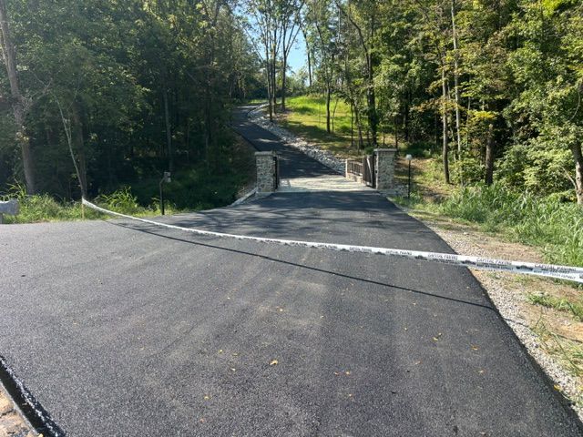 Paved road blocked by a downed cable, leading uphill through a wooded area