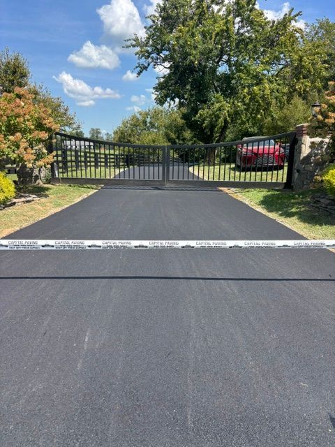 Black driveway with speed bump leading to a closed metal gate under a blue sky.