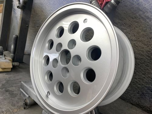 Silver alloy wheel rim with multiple circular cutouts, leaning against a wall in a workshop.