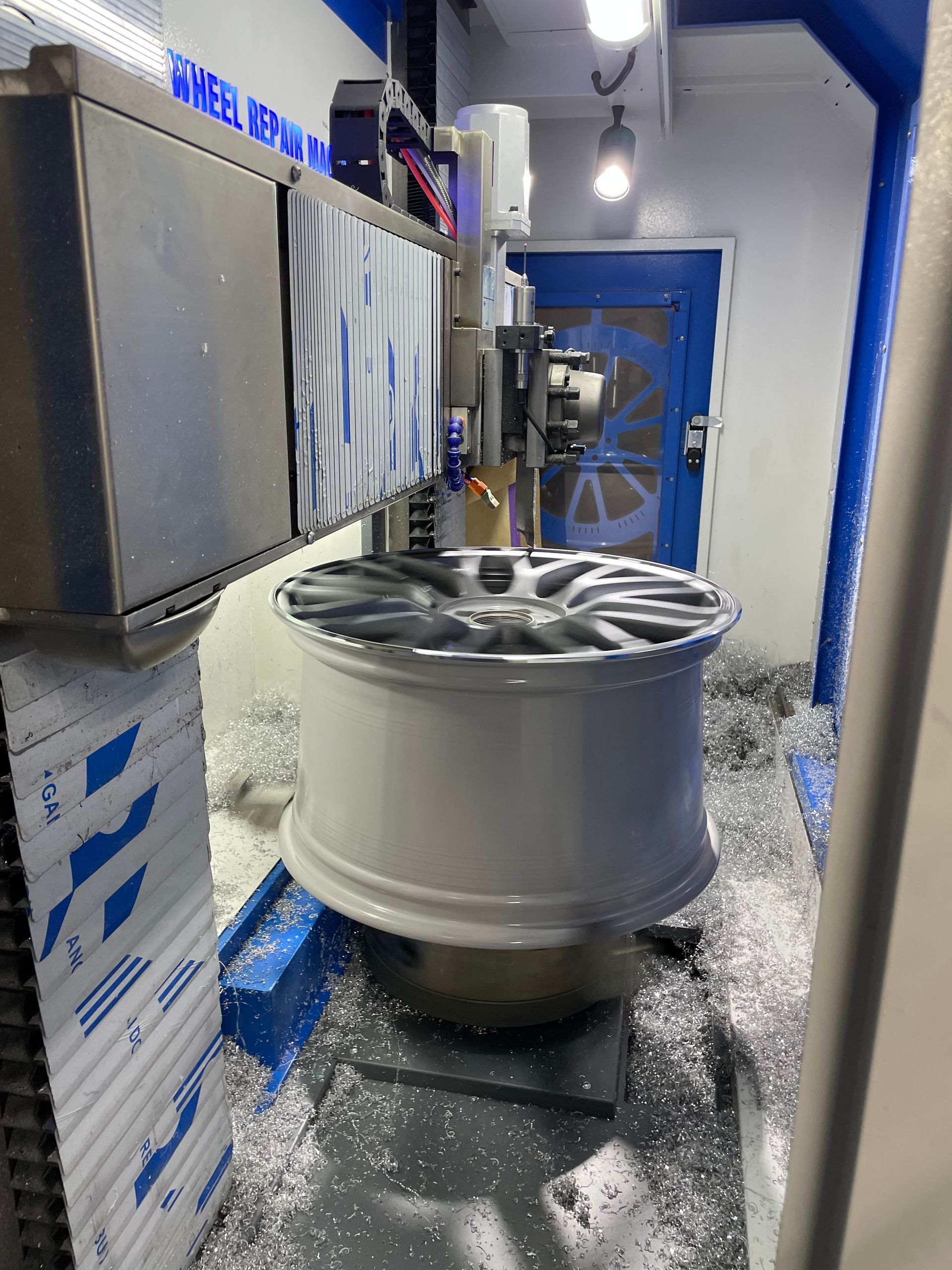 White alloy wheel in a blue auto workshop, with metal shavings scattered on the floor.