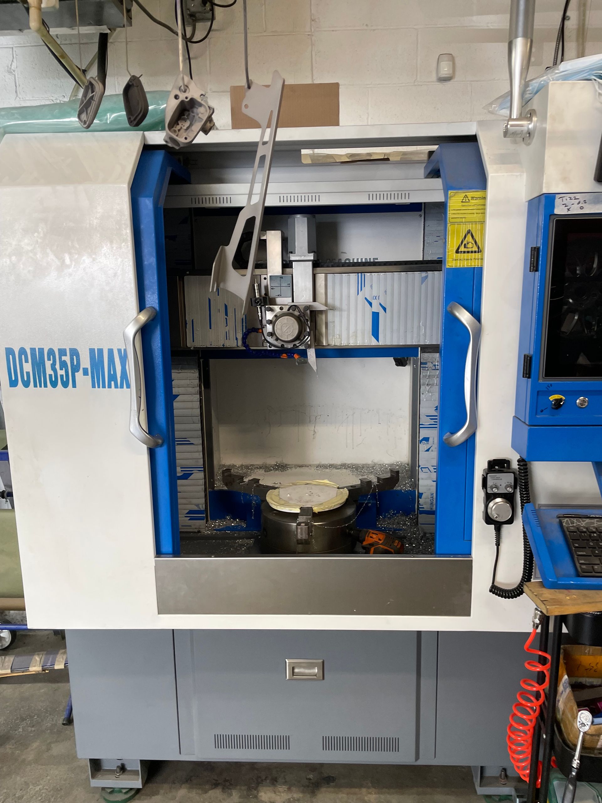 Blue and white CNC machine in a workshop, with open front door and control panel on the right.