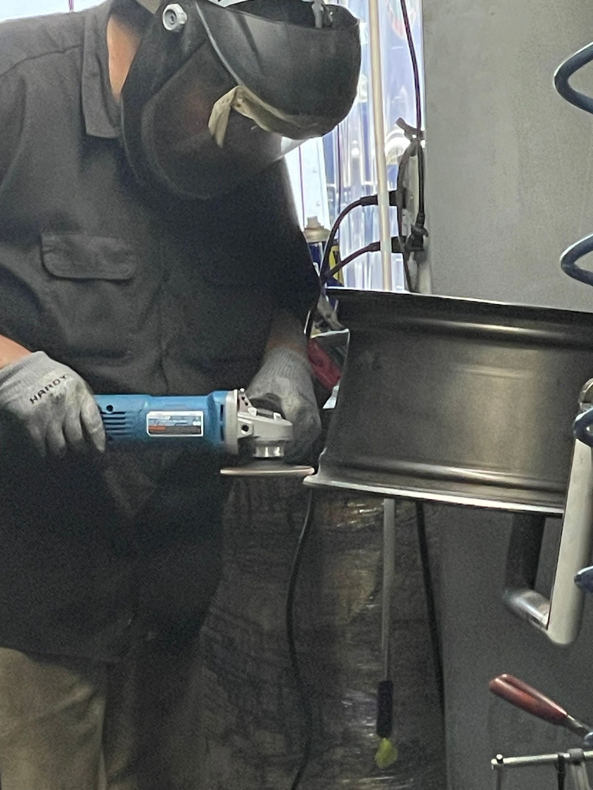 Worker grinding a metal drum with a power tool while wearing a face shield and gloves