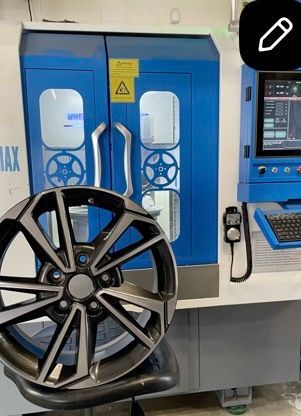 Black alloy wheel rim displayed in front of a blue industrial machine in a workshop