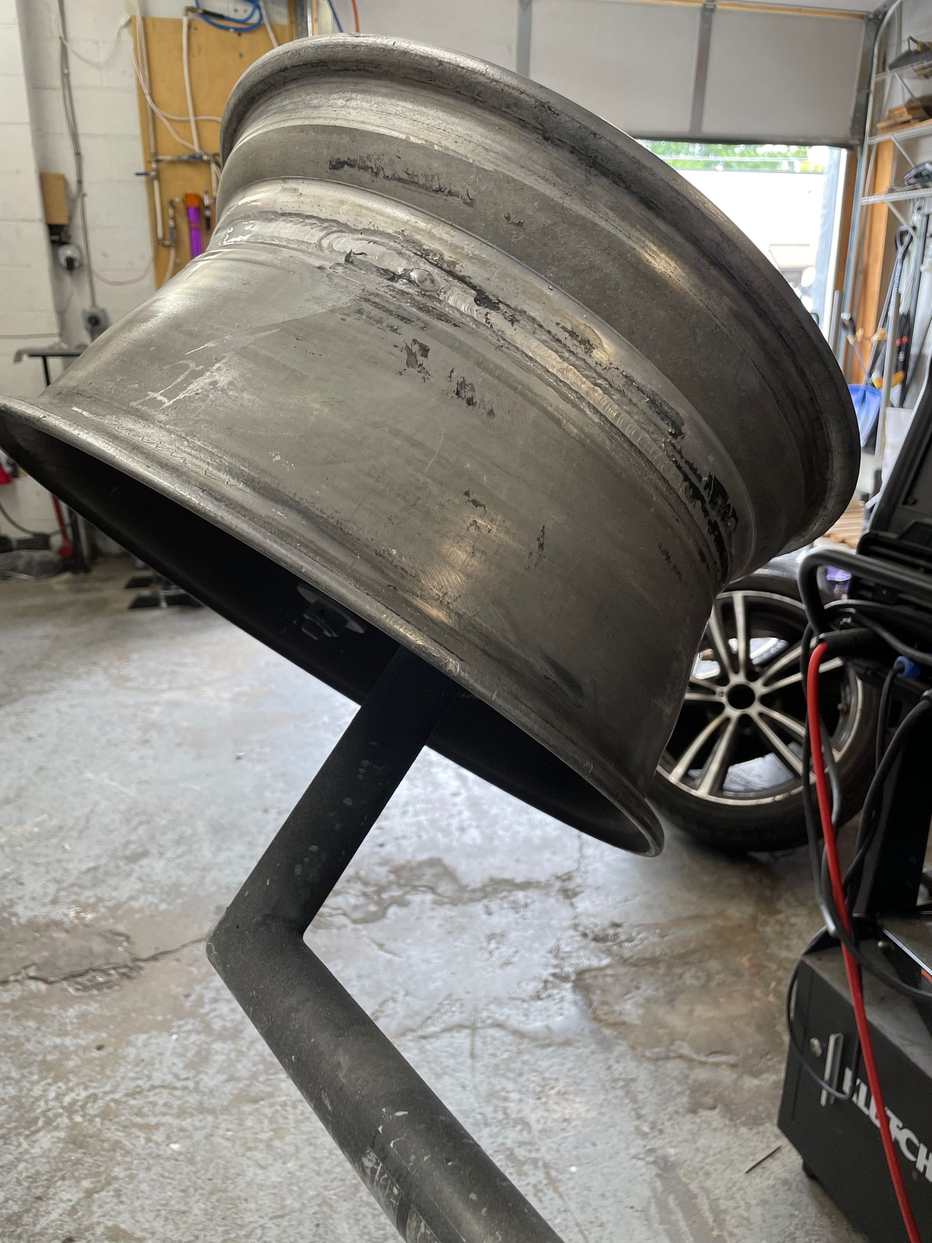 Large black metal wheel rim propped on a stand in a garage workshop.