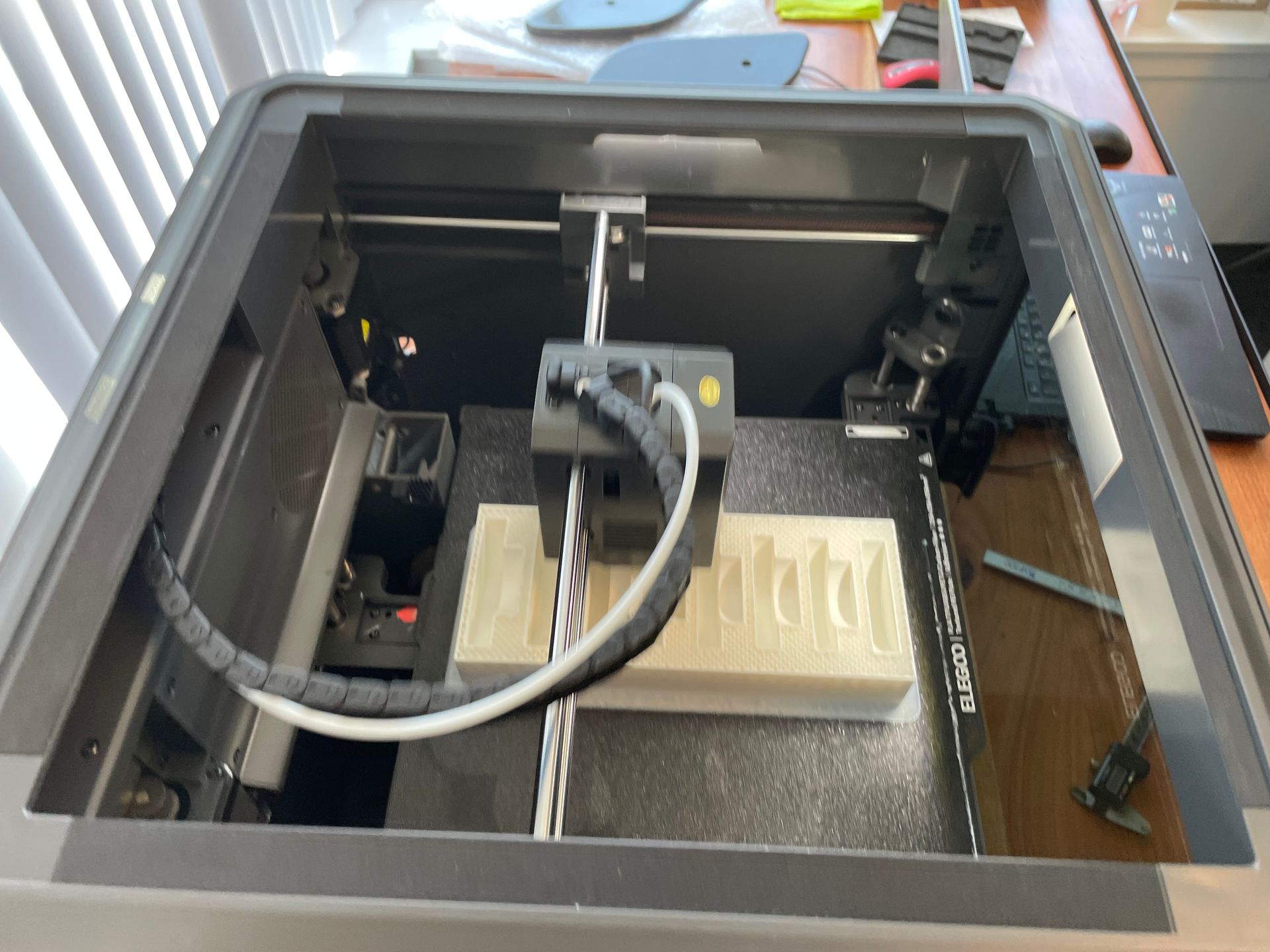Open 3D printer interior with a white print on the build plate and a gray cable assembly above it