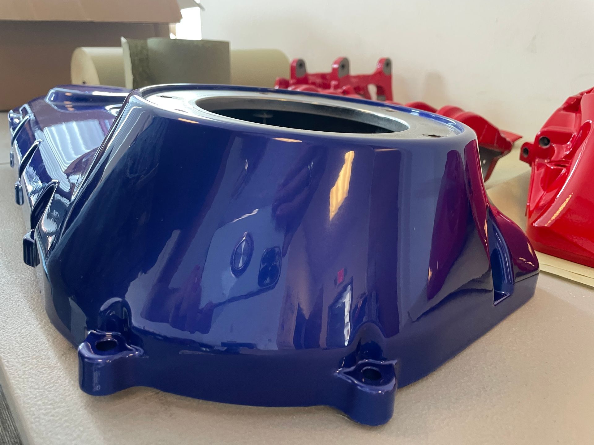 Blue glossy plastic automotive part with a circular opening, resting on a table.