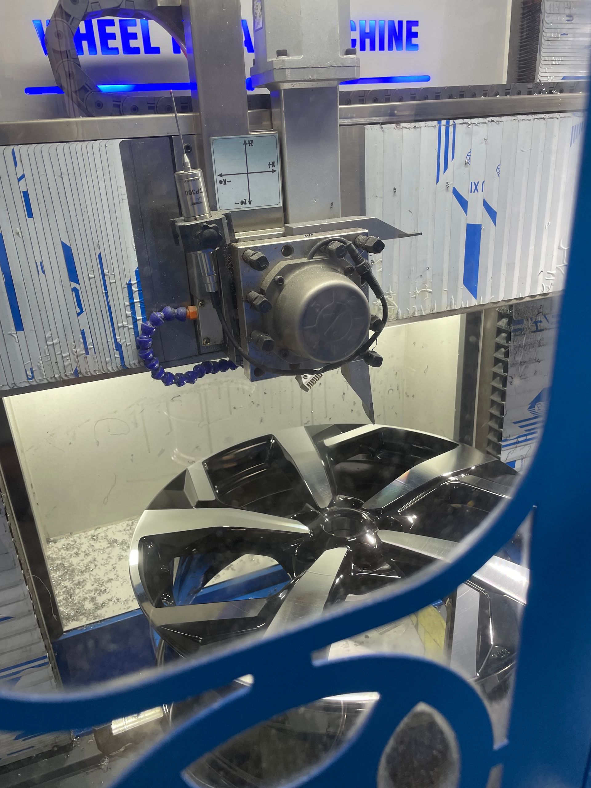 CNC machine milling a black wheel rim inside an industrial shop
