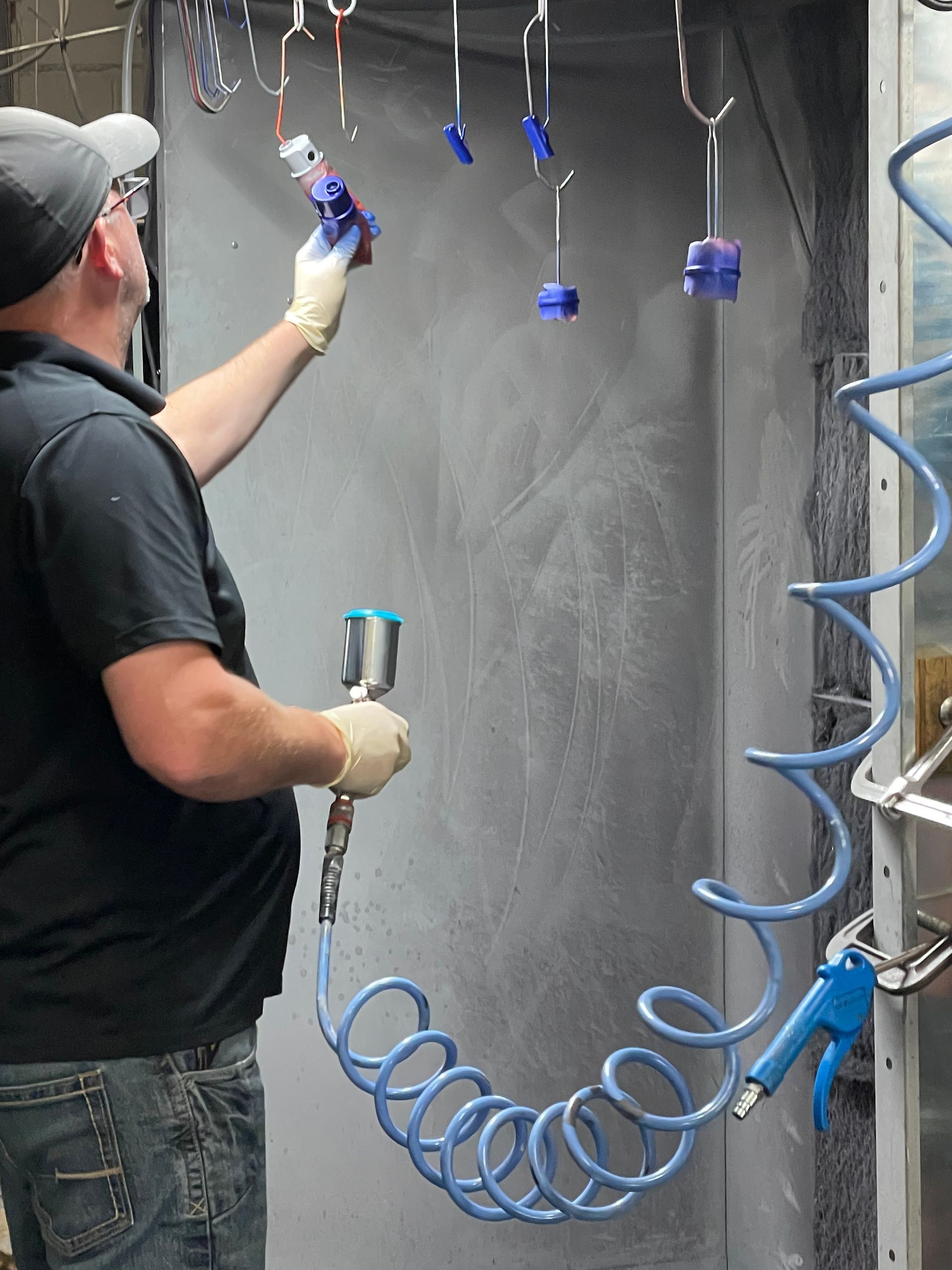 Worker spray-painting a large gray wall with a blue air hose attached to a paint gun