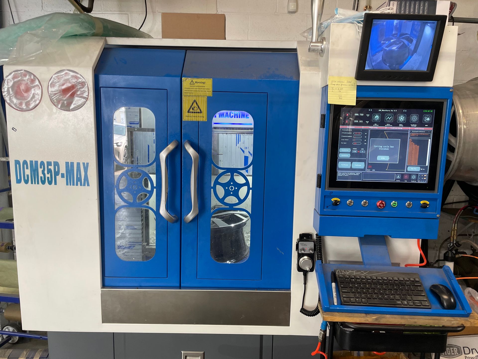 Blue-and-white industrial machine with a control screen and keyboard in a workshop