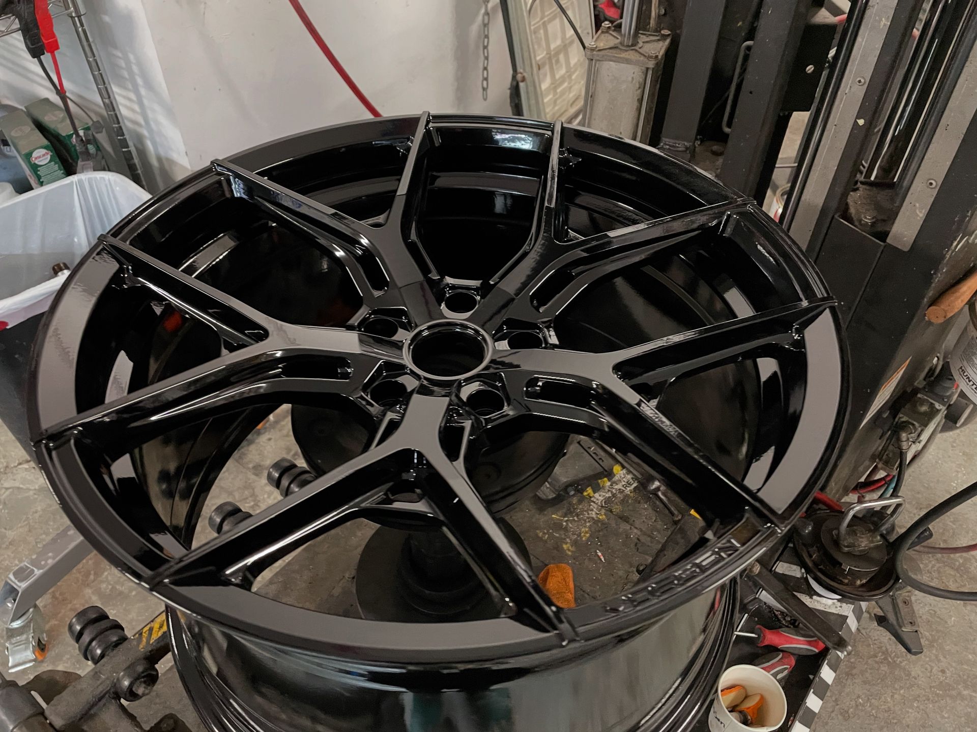 Glossy black alloy wheel rim sitting on a workshop tire-changing machine