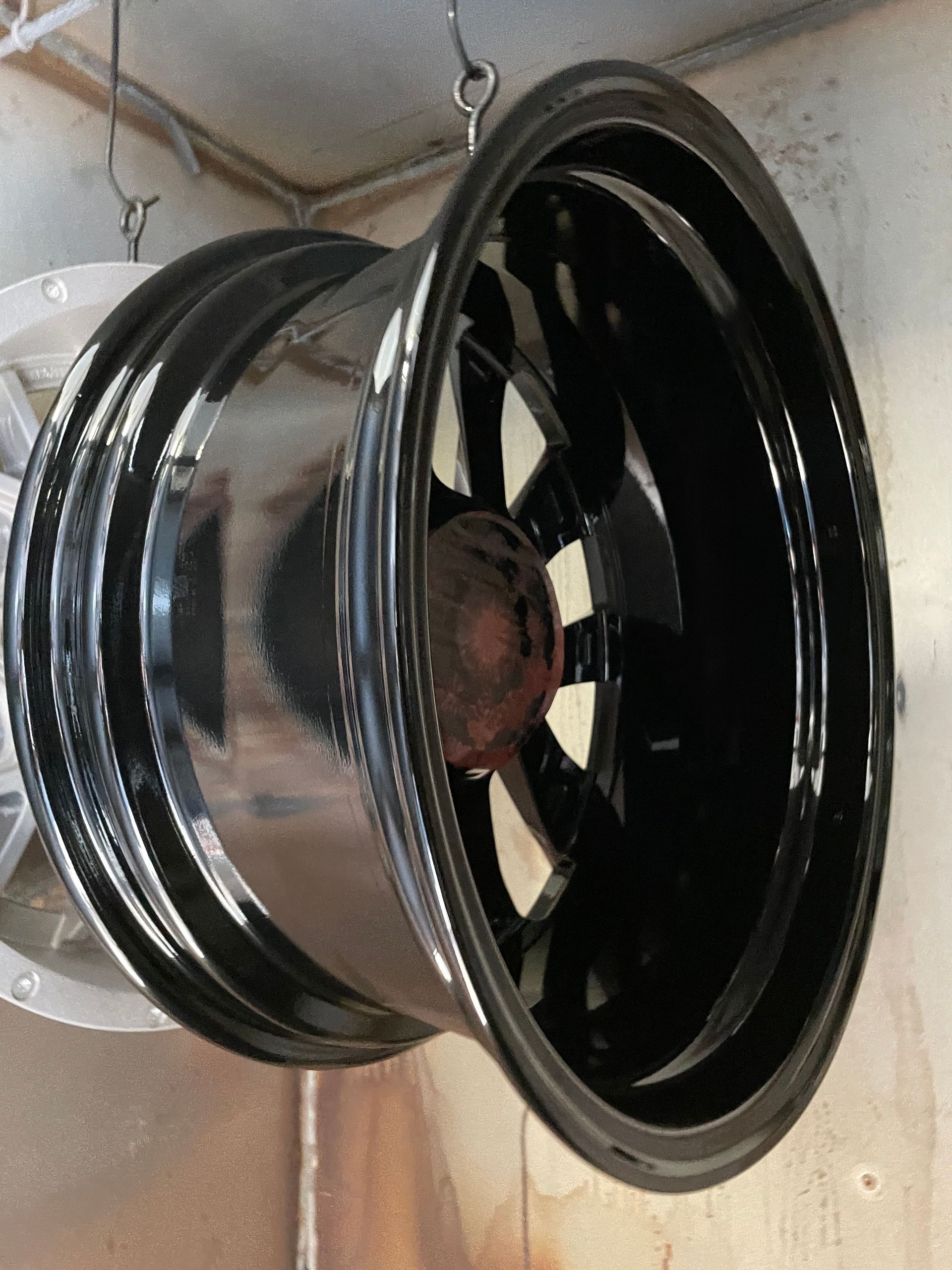 Black car wheel rim with a silver center, leaning against a wall in a workshop.