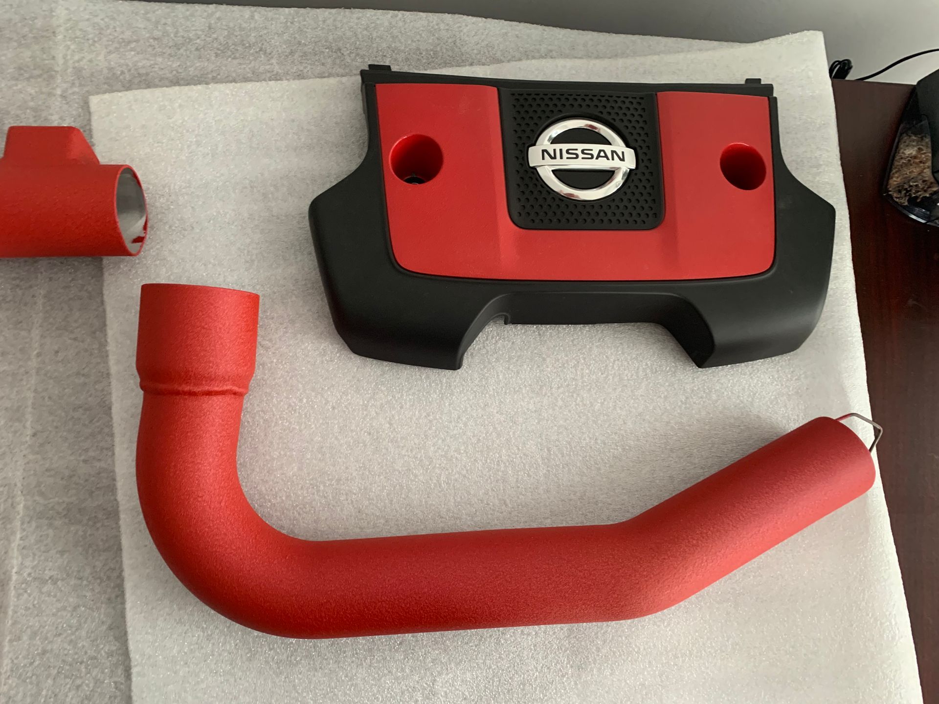 Red Nissan intake tubing and black-red engine cover parts arranged on a white surface.