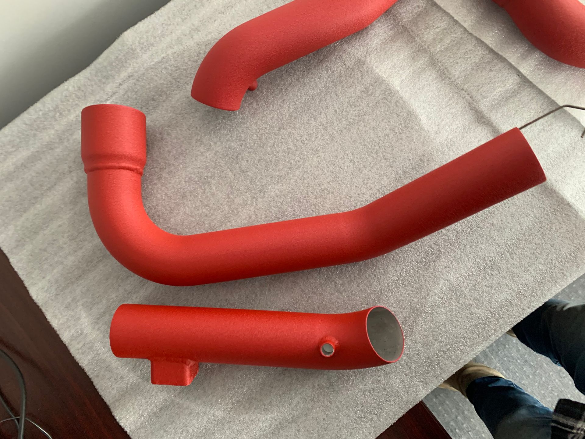 Red painted metal pipes and fittings laid on a gray towel.