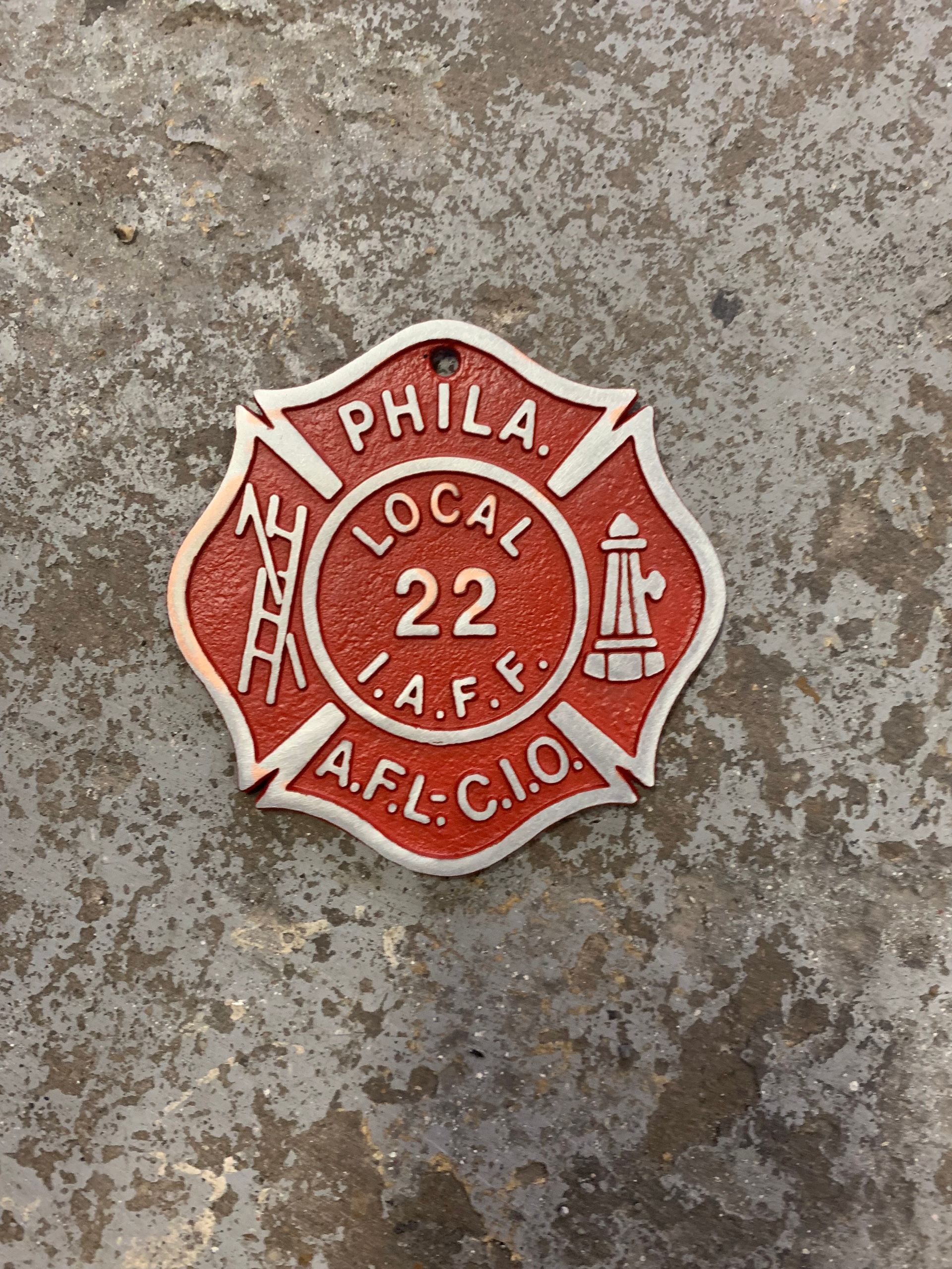 Red Philadelphia I.A.F.F. Local 22 fire badge on weathered gray concrete.