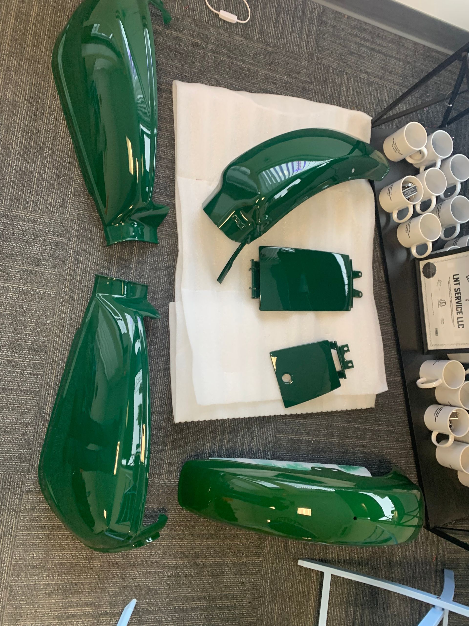 Green car body parts and small components laid out on a floor for painting or assembly