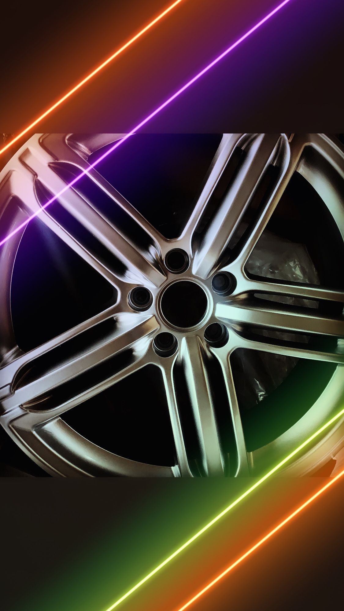 Close-up of a chrome alloy wheel rim with neon pink, purple, and green light streaks on a dark background