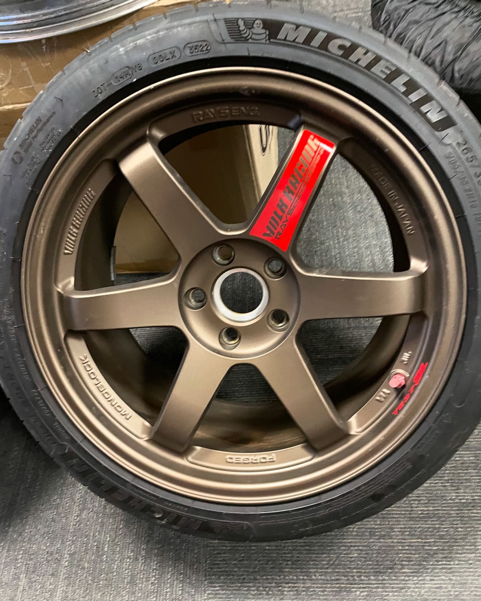 Bronze five-spoke MICHELIN tire and wheel on a carpeted floor, with a red sticker on the rim.