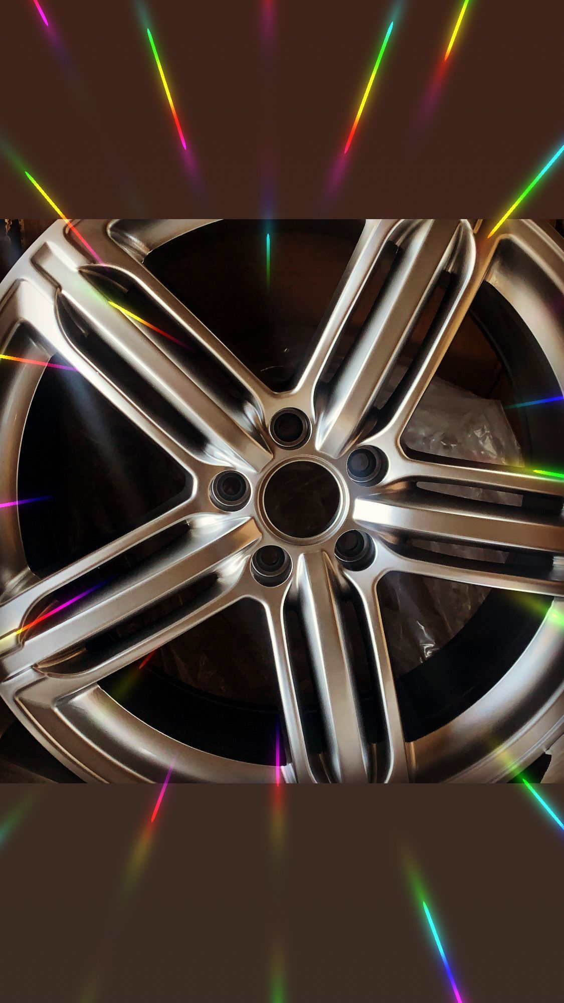 Shiny chrome alloy wheel rim with five spokes, reflecting colorful light streaks on a dark background