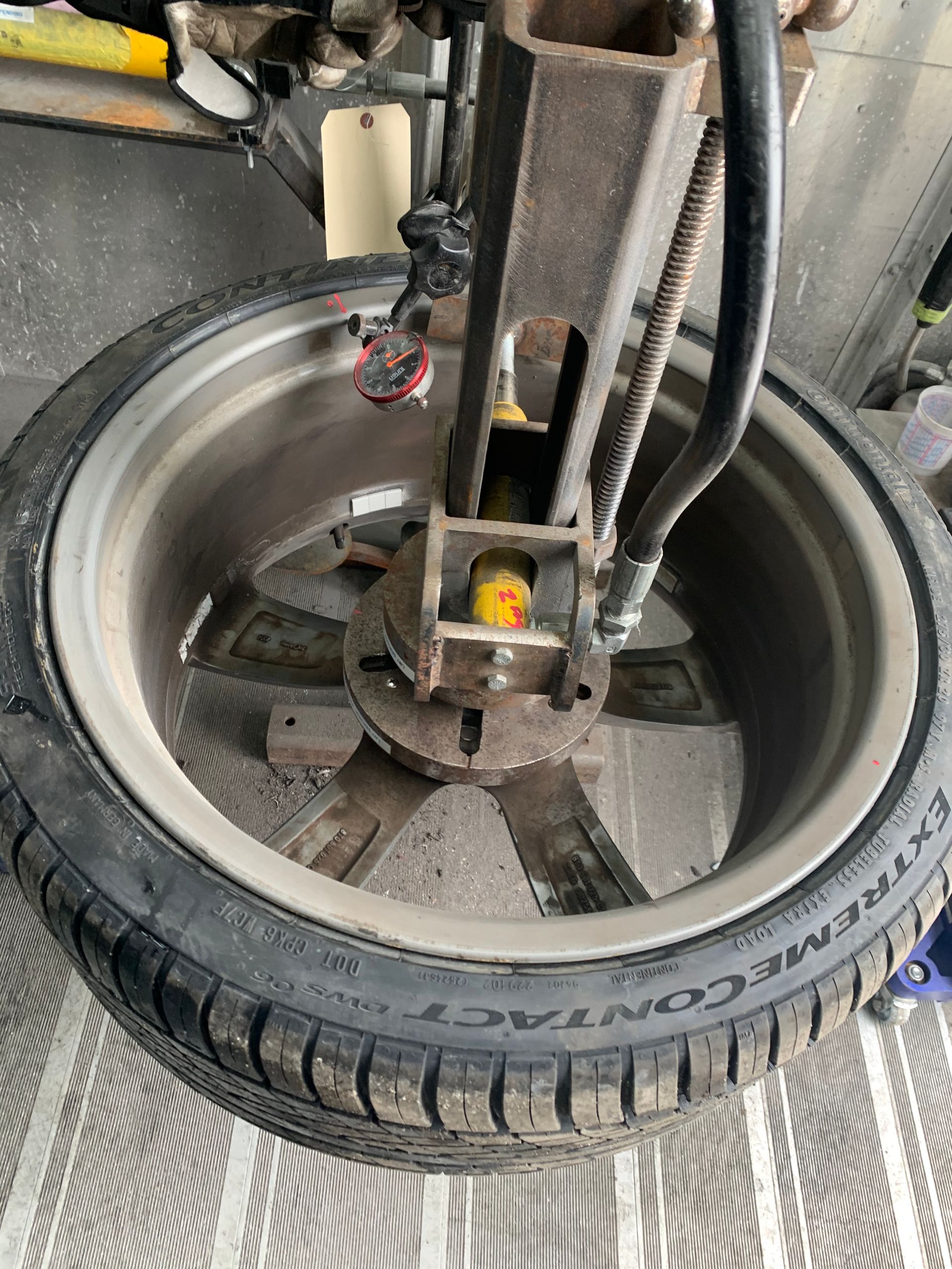 Close-up of a bicycle wheel and spokes with a tire, cable, and metal frame in a garage-like setting