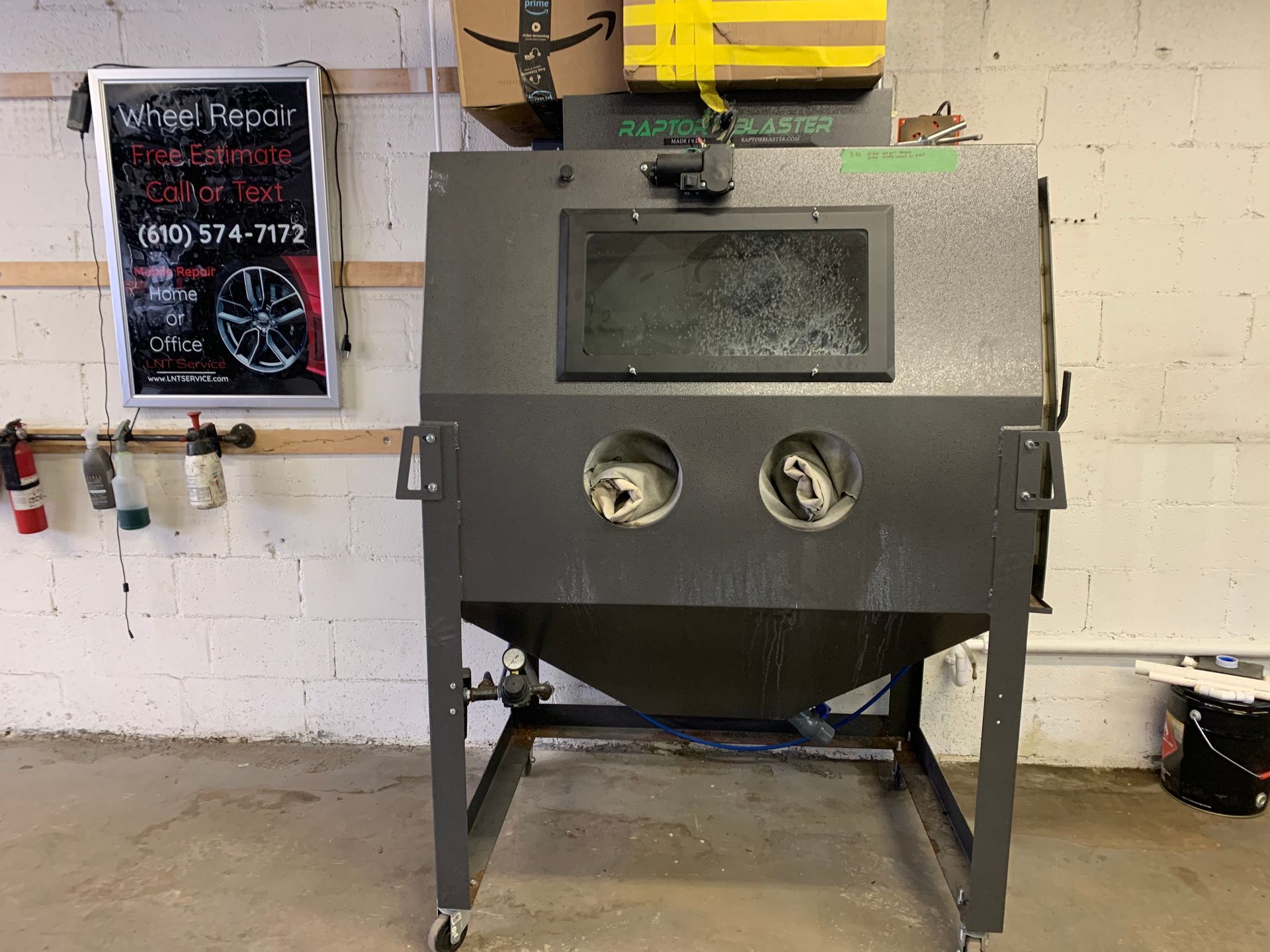 Gray sandblasting cabinet in a workshop, with two round viewing ports and a front window.