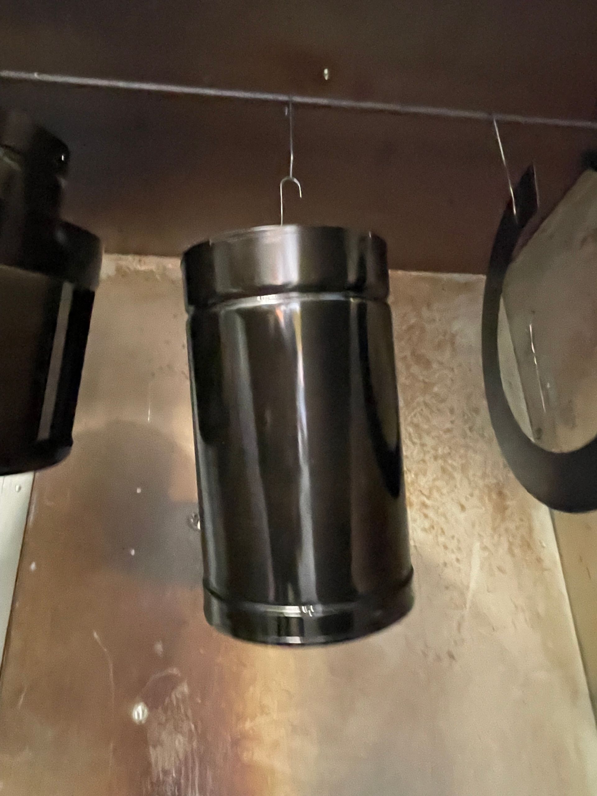 Black cylindrical trash can under a counter in a beige kitchen area