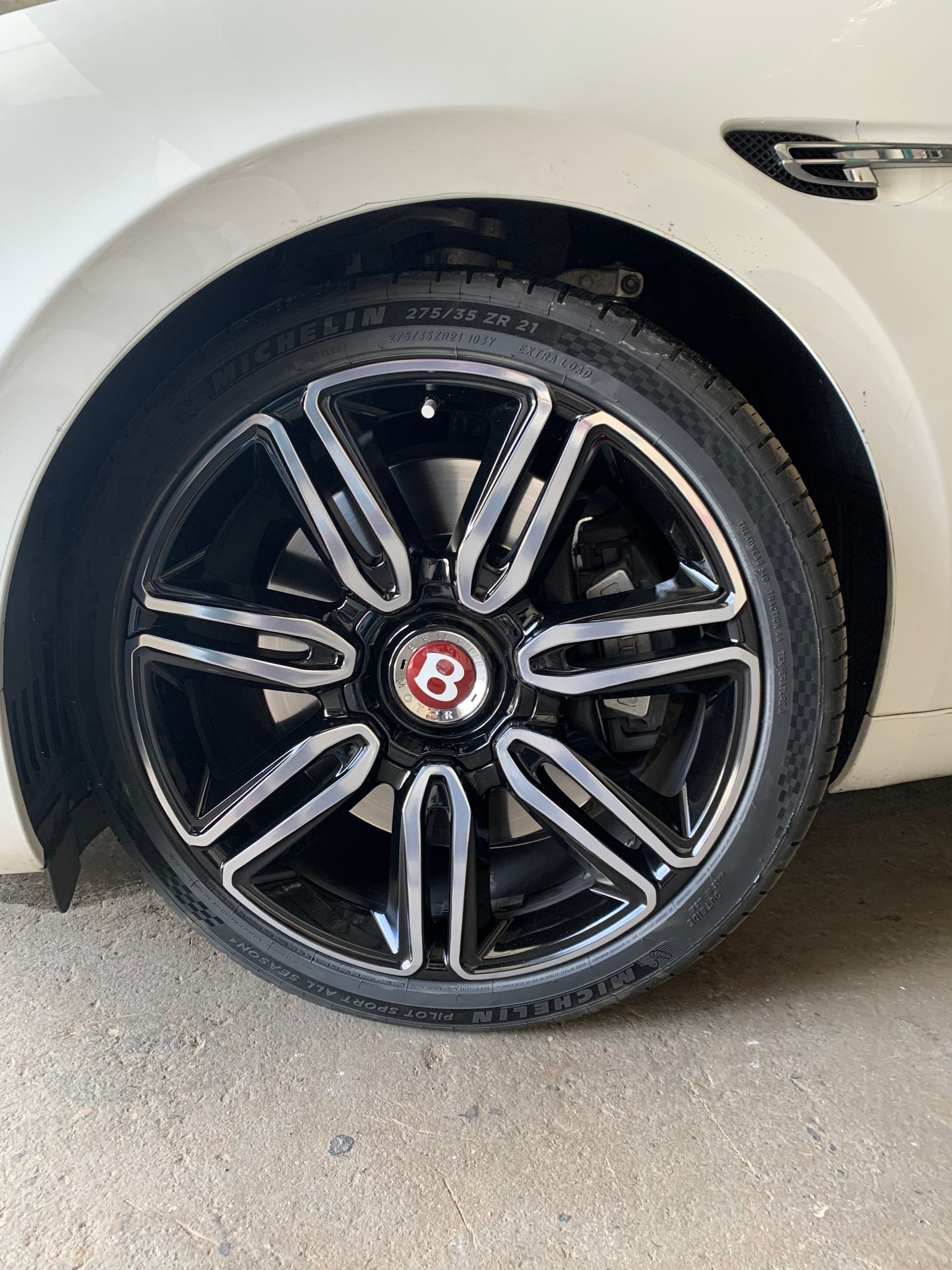 Black Bentayga wheel with red “B” badge on a white vehicle parked on pavement