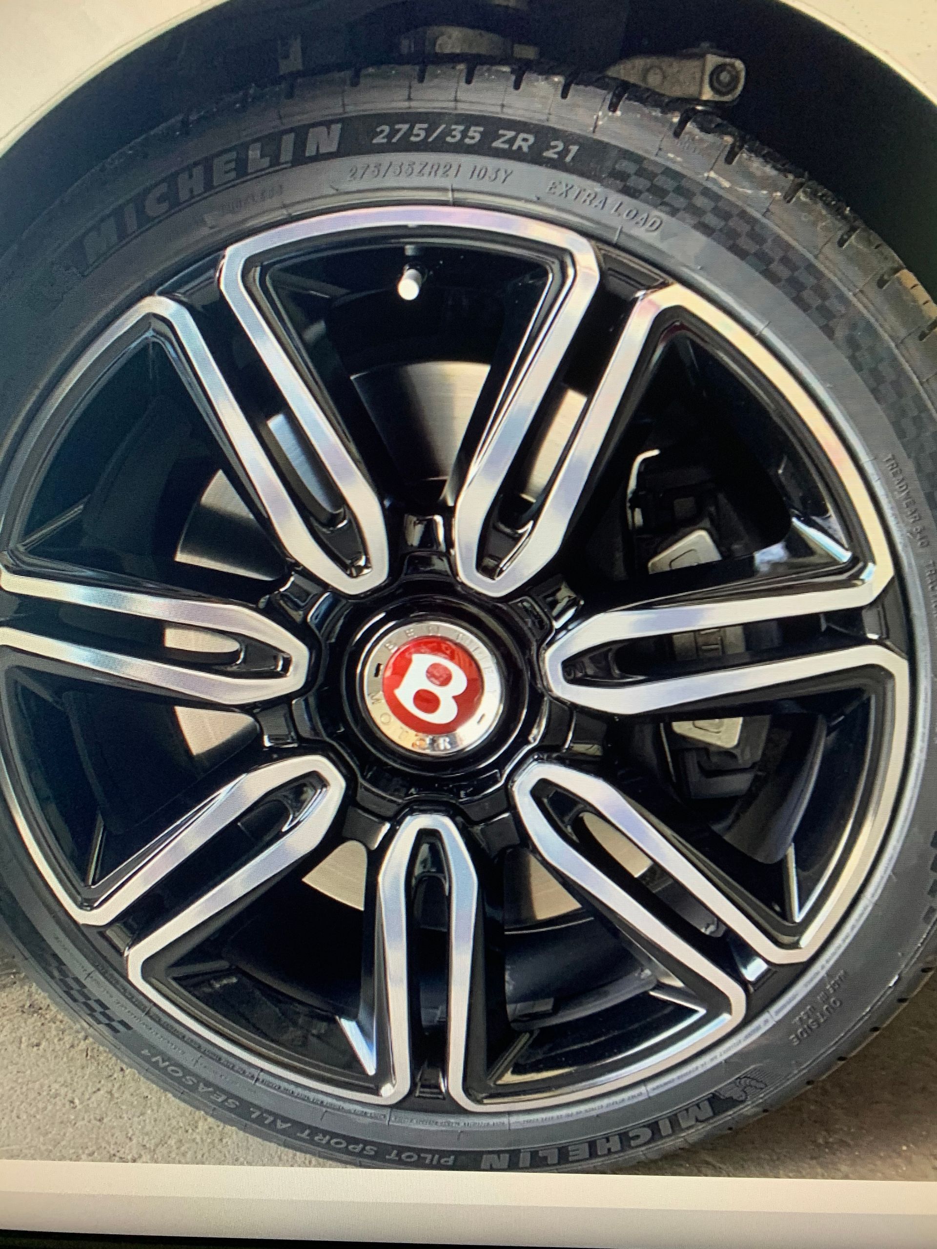 Close-up of a black and silver Bentley alloy wheel with a red center emblem and tire.