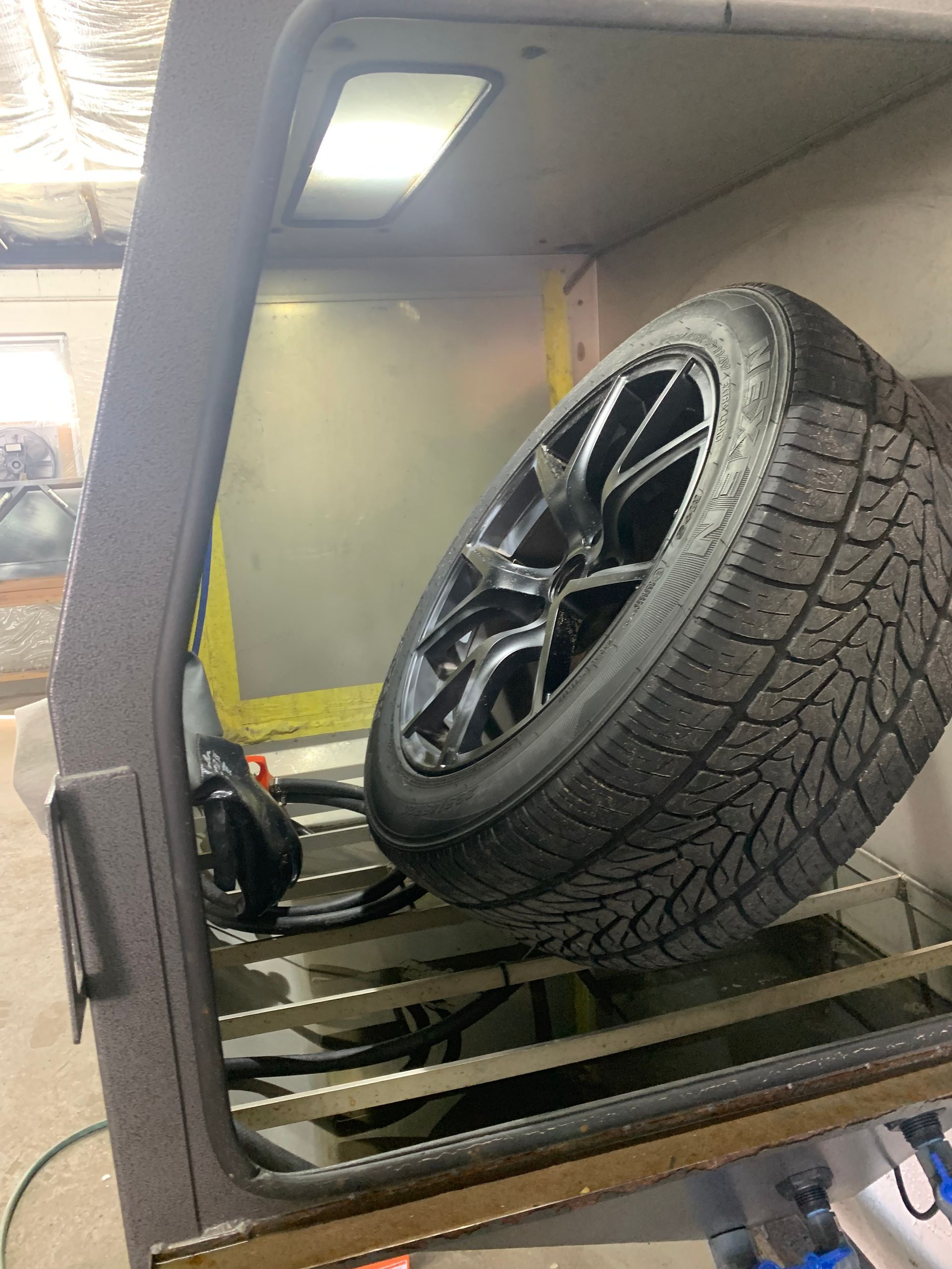 Car tire mounted on a black alloy wheel inside a vehicle or shop bay.