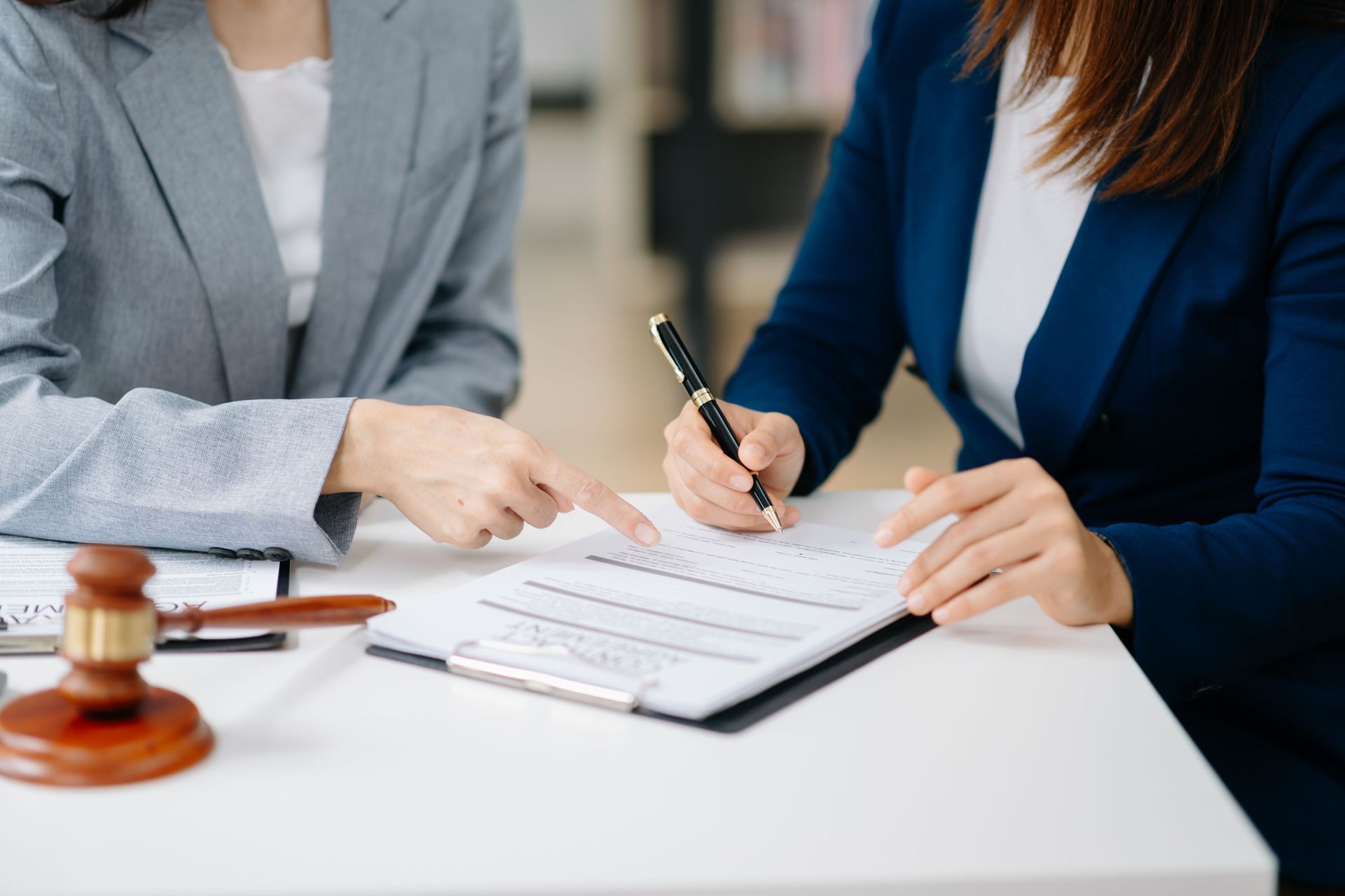 Two people in suits reviewing paperwork, one pointing, the other writing. Gavel on the table.