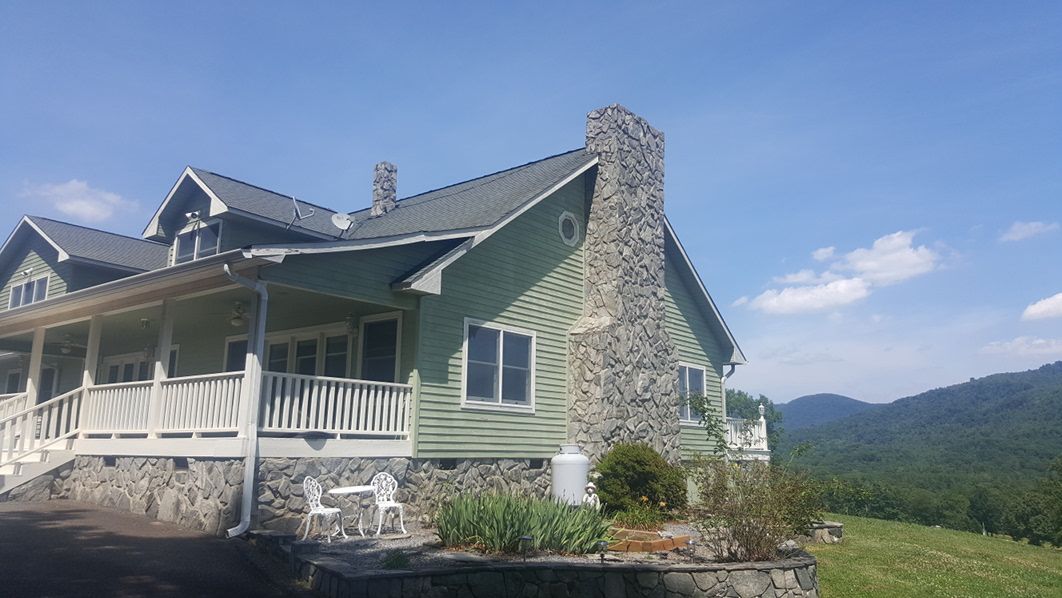 A large green house with a large porch and mountains in the background.